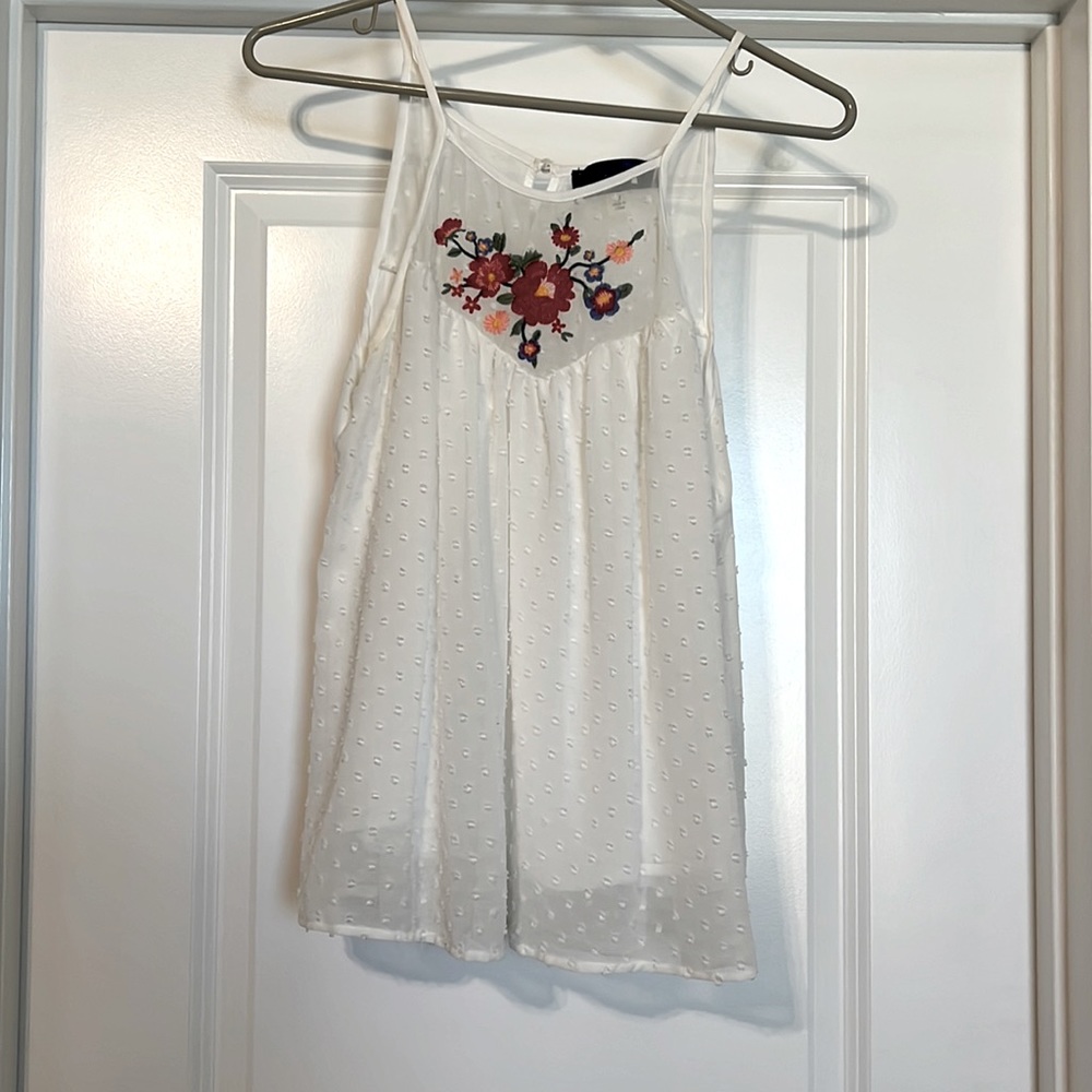 White tank top with flower detail neckline. Has a  dotted texture.